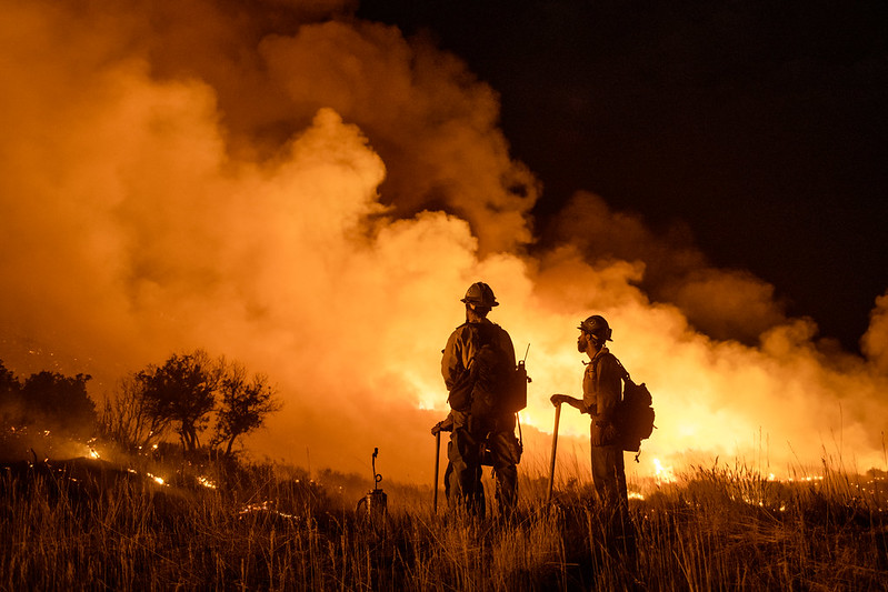 Photo of two firefighters talking in front of Pine Gulch fire at night